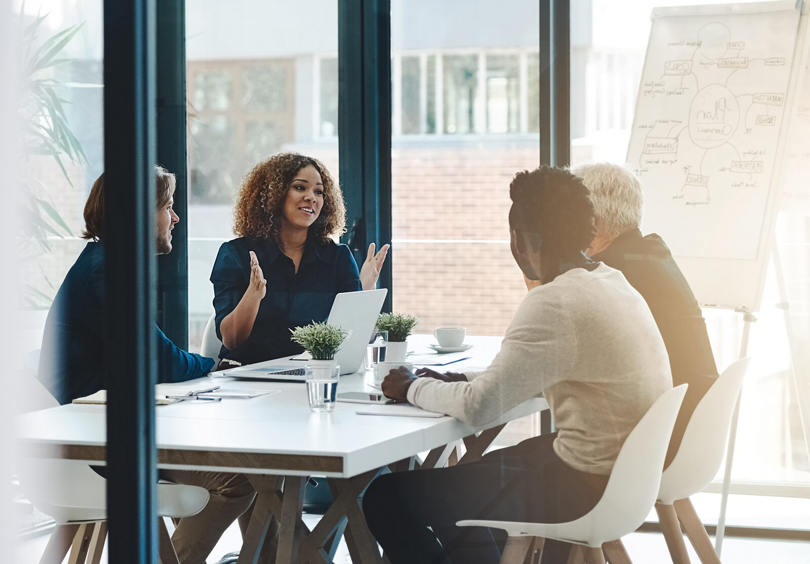Colleagues discussing around a conference table with a laptop, seen through a glass wall