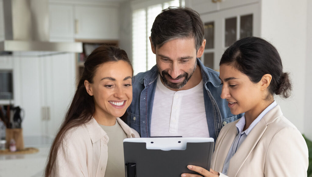 Real estate agent reviewing a clipboard with a couple in a bright home