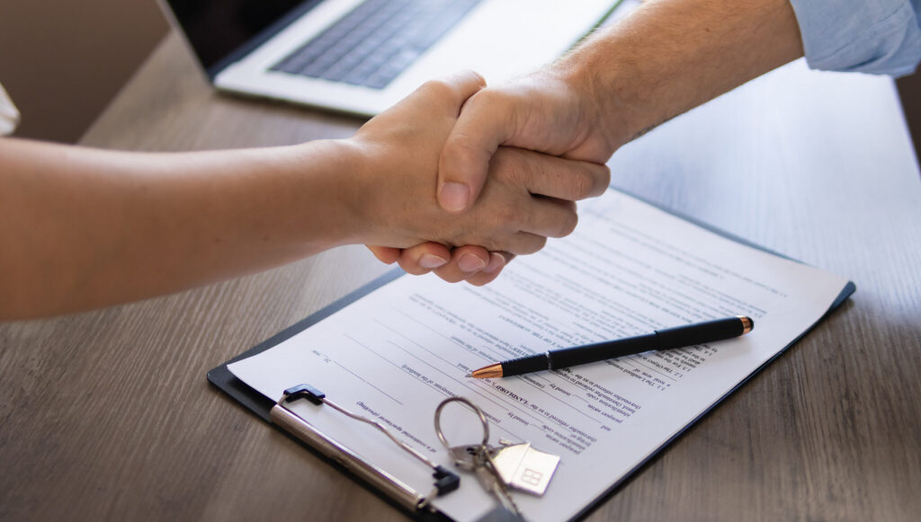 Handshake over a signed agreement with a house-shaped key tag on a clipboard