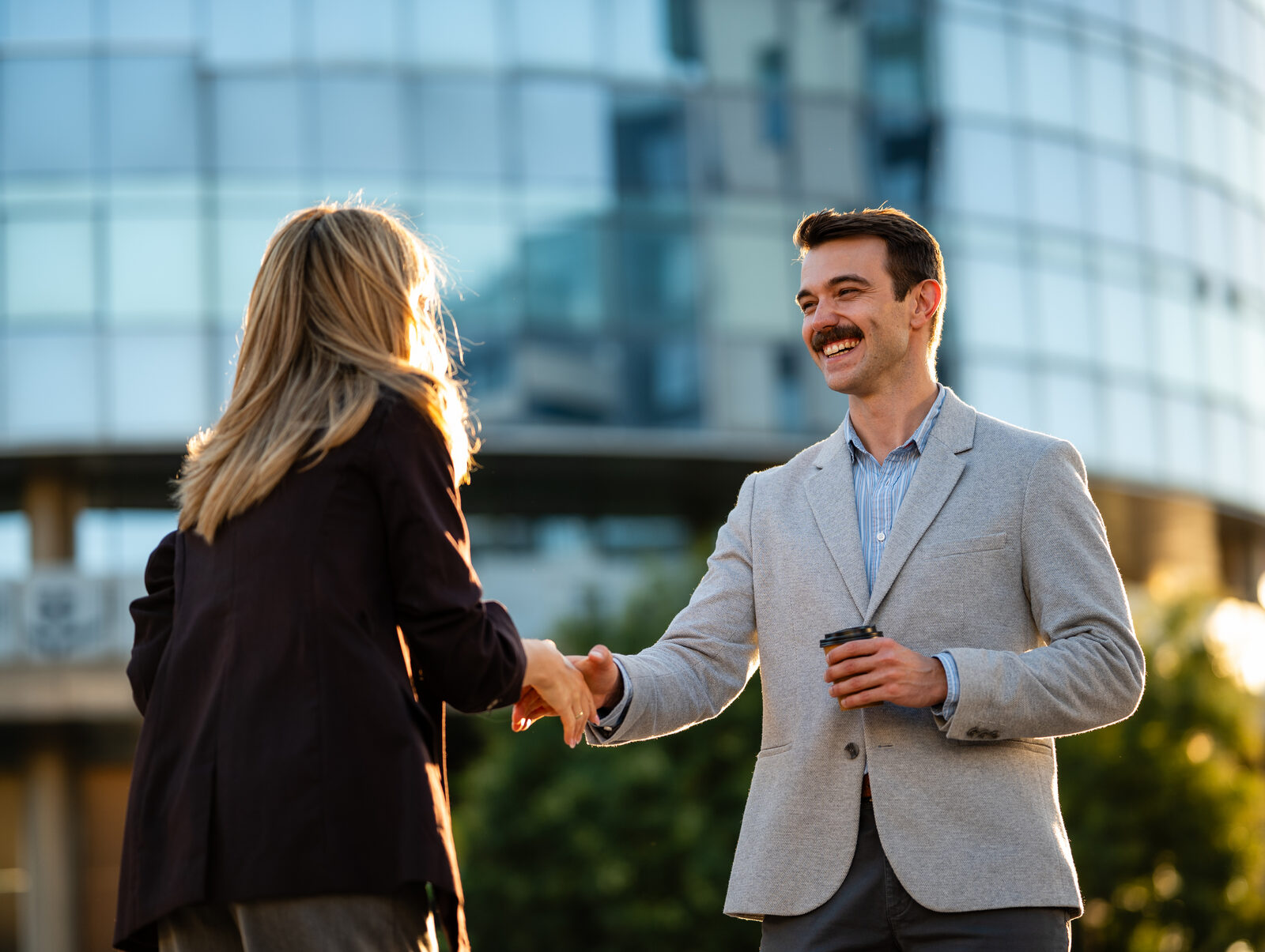 Two professionals greeting each other with a handshake outside an office building