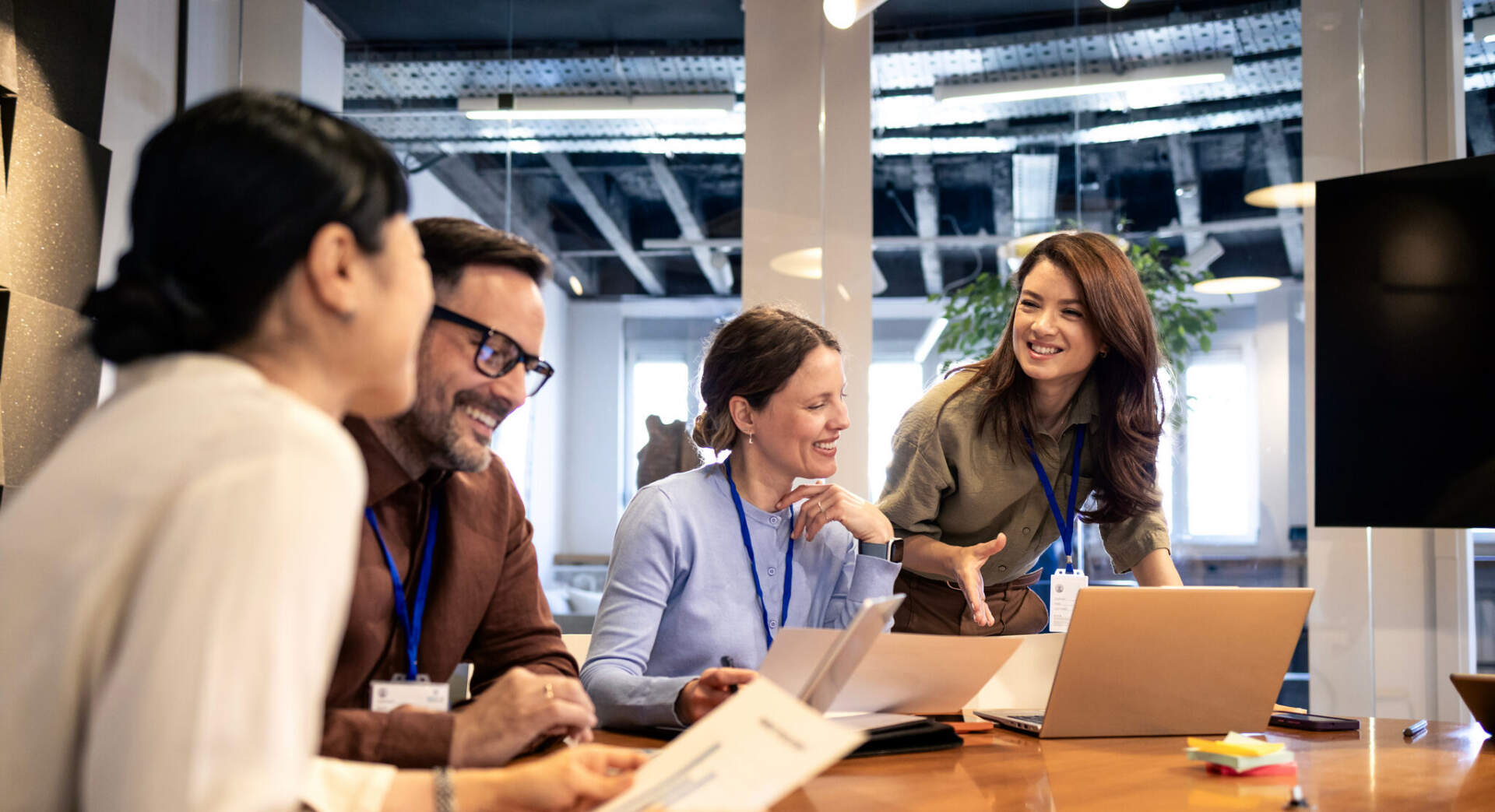 Colleagues smiling and collaborating around a table with laptops
