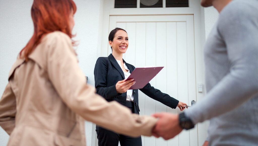 Real estate agent with a clipboard greeting a couple at the front door of a home