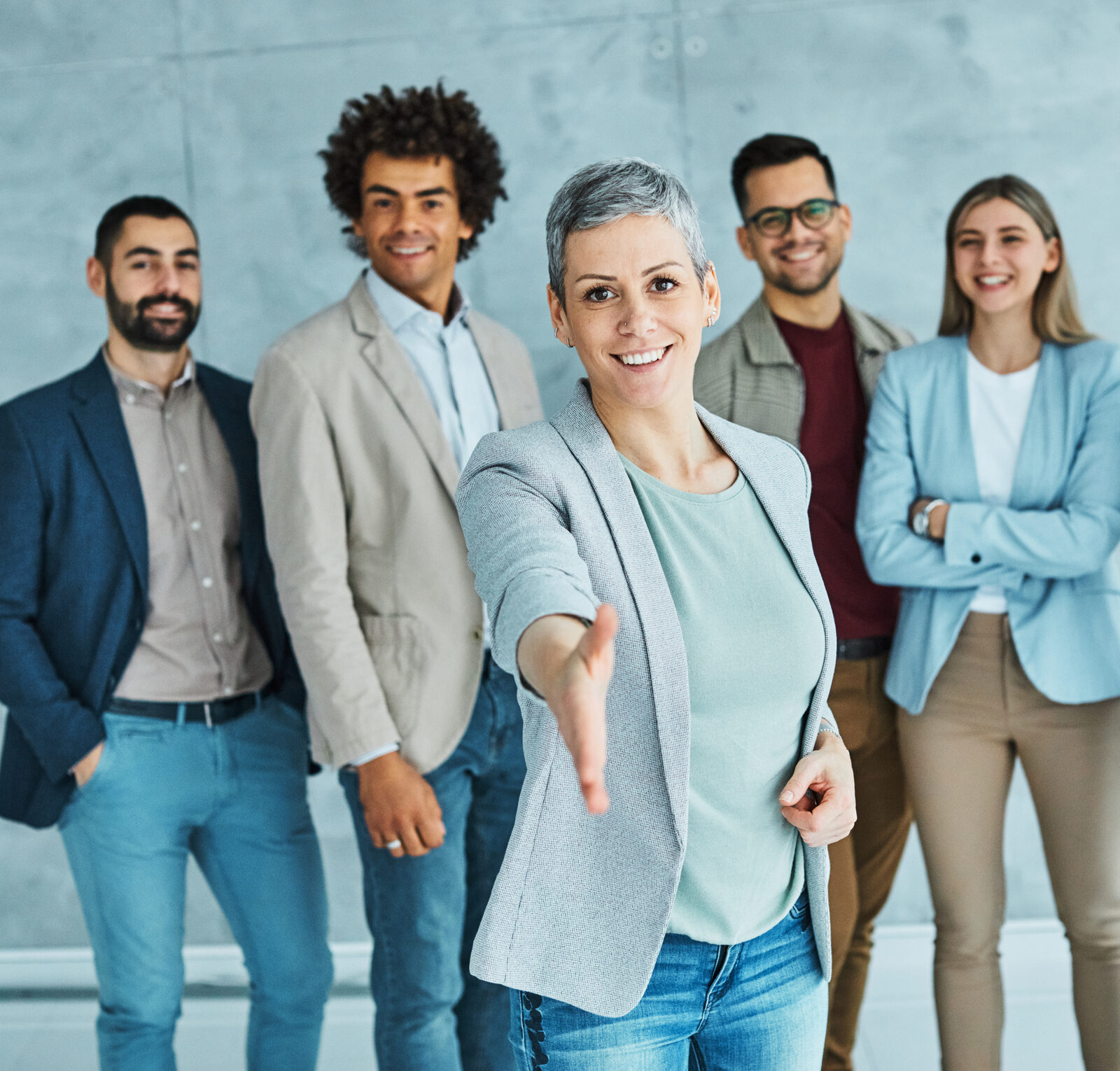 A team of five smiling professionals, one offering a handshake