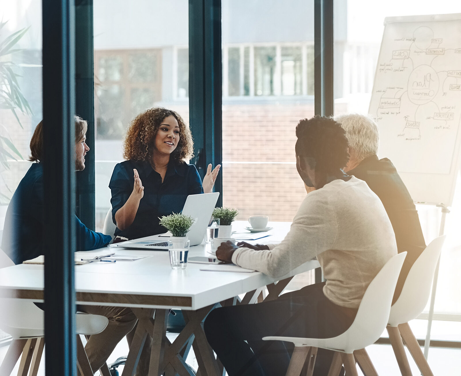 Colleagues discussing around a conference table with a laptop, seen through a glass wall
